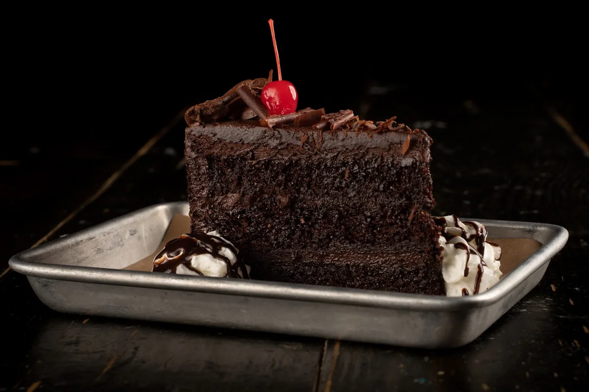 Giant chocolate cake slice, three layers with piped rosettes and a cherry